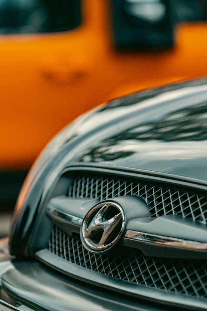 Sharp image focusing on a car grille with a yellow vehicle in the background, capturing urban details.